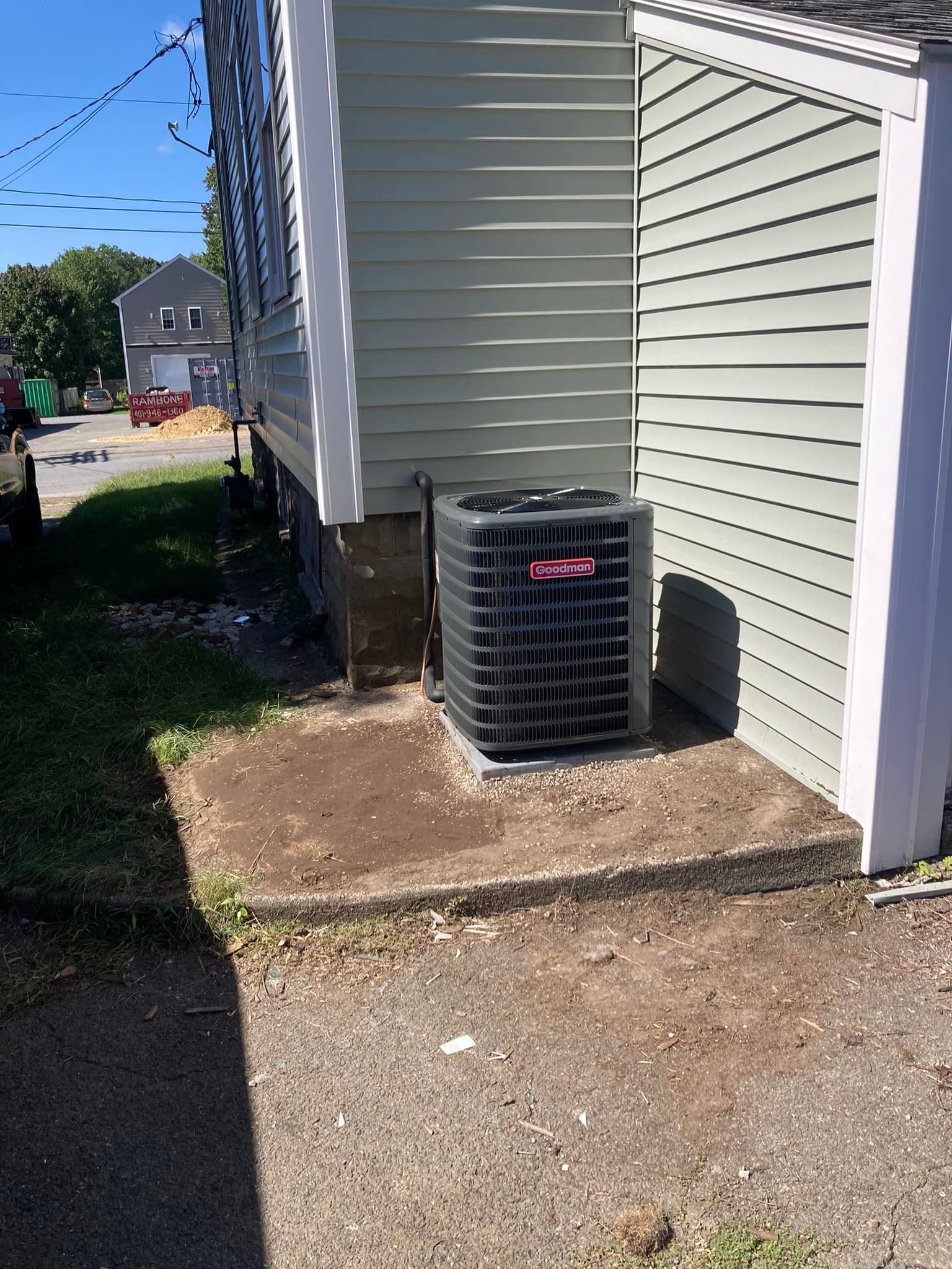 Outdoor air conditioner unit beside a house on a gravel side yard with a narrow walkway