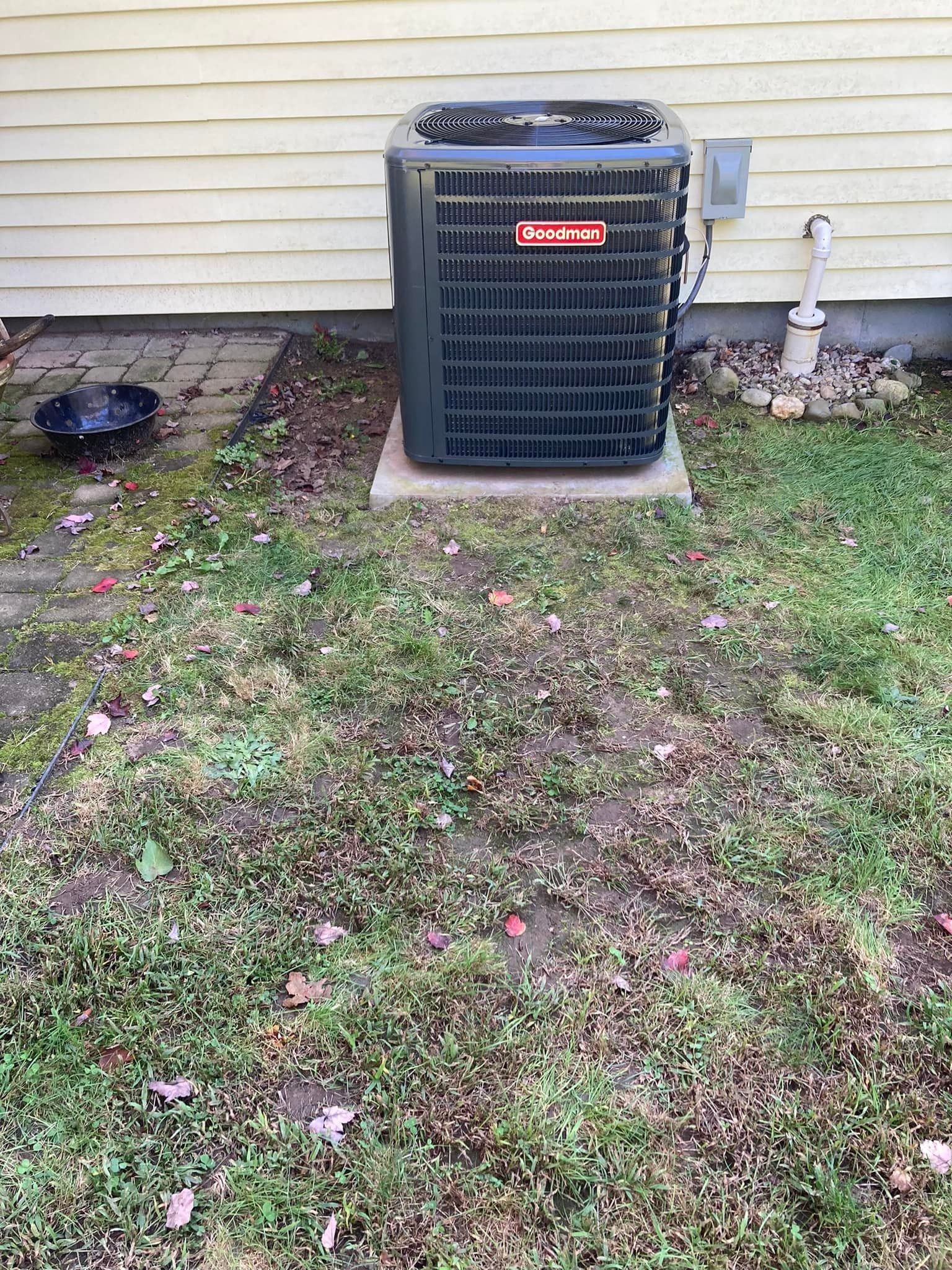 Backyard HVAC unit beside a house wall, with grass and a concrete pad.