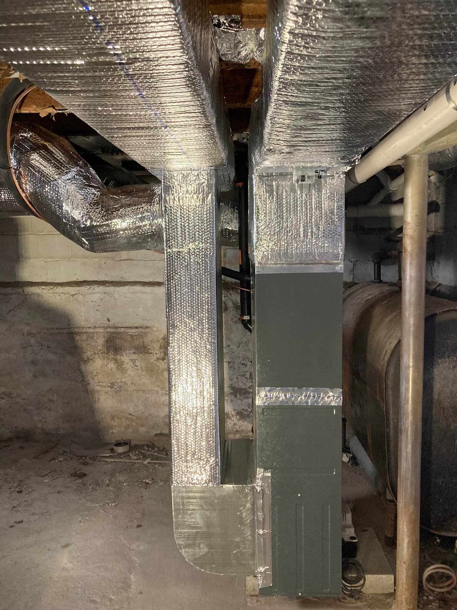 Metal HVAC ductwork and insulated pipes in a basement mechanical room.