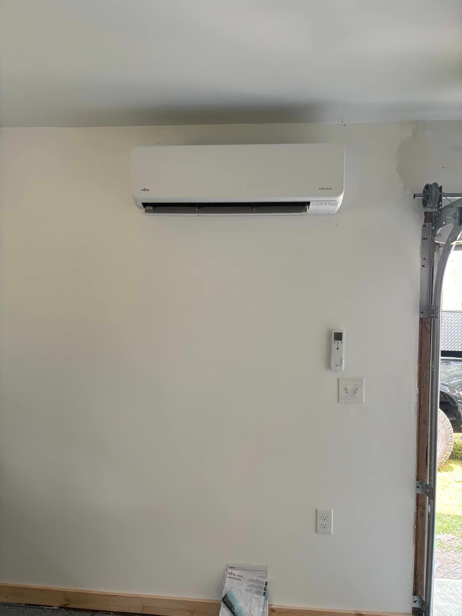 Wall-mounted white air conditioner on a beige wall in a room with a window and light switch.