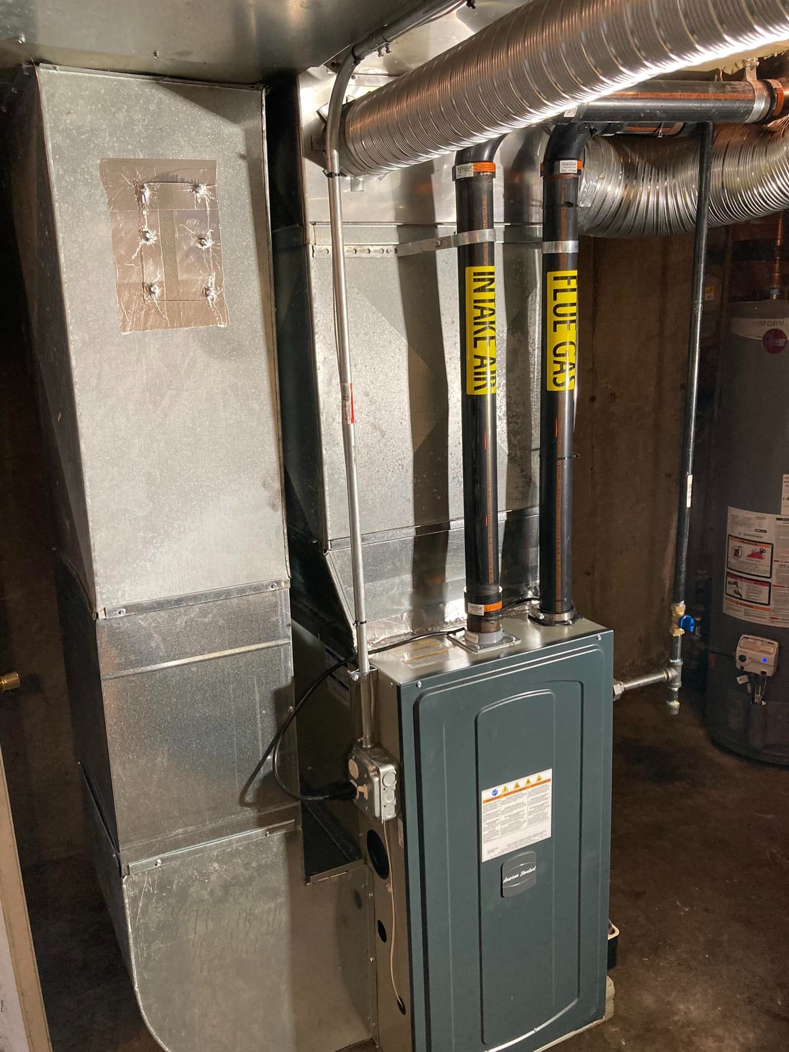Basement utility room with gray HVAC ducting, pipes, and a green electrical panel.