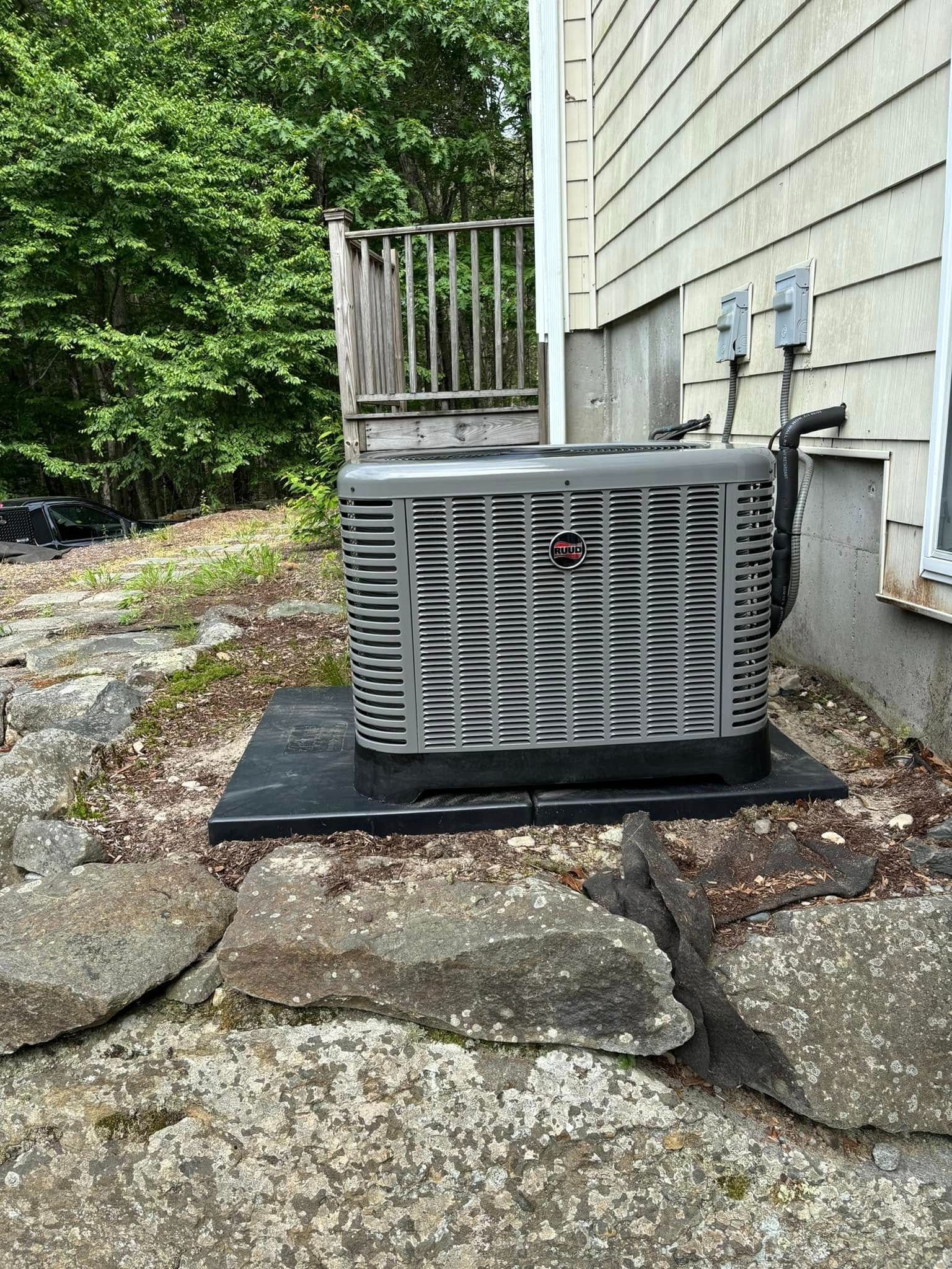 Outdoor air conditioner unit beside a house on a stone and gravel base