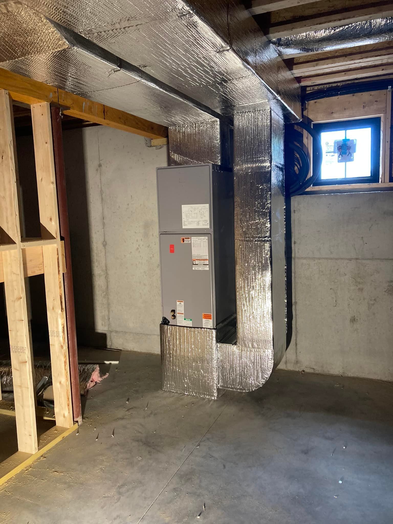 Basement utility area with HVAC ducting, electrical panel, exposed framing, and a small window.
