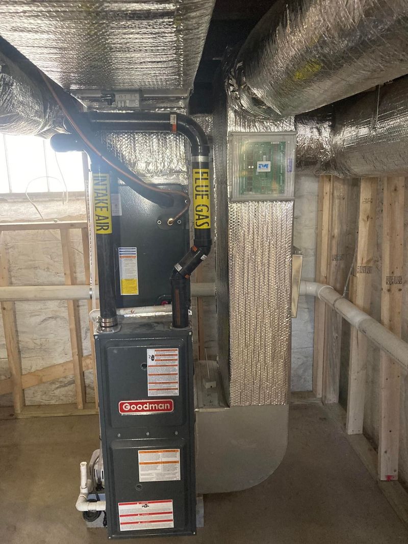 Black HVAC unit and insulated ductwork in a basement utility area under construction