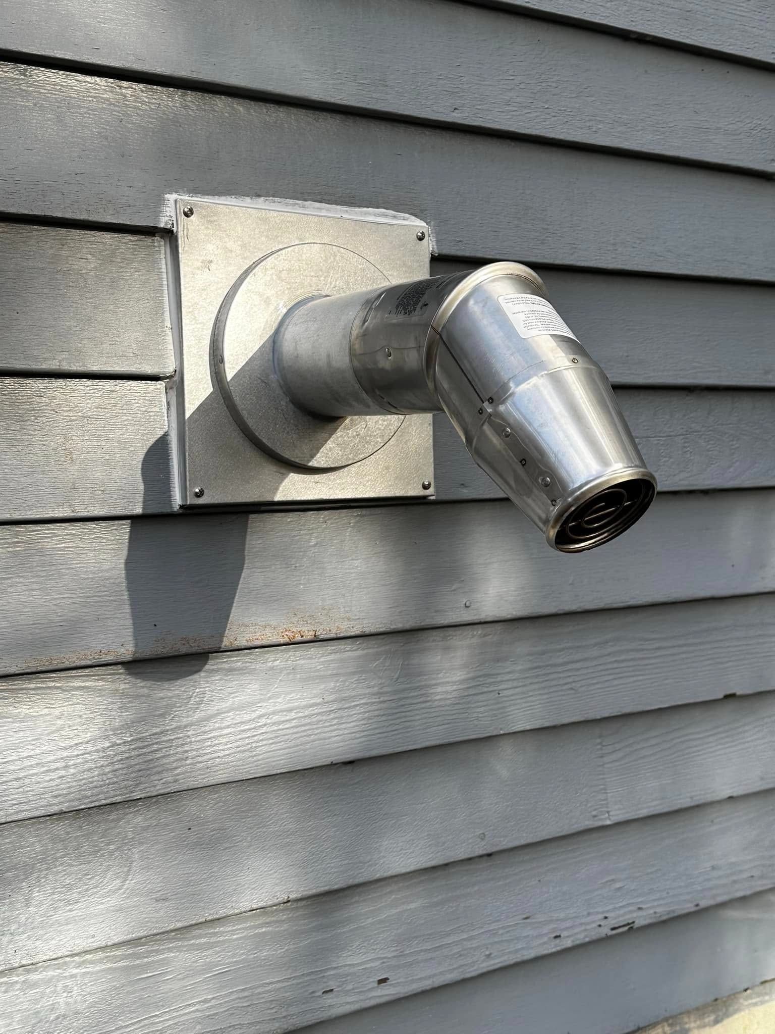 Chrome vent pipe protruding from gray house siding near a square wall plate