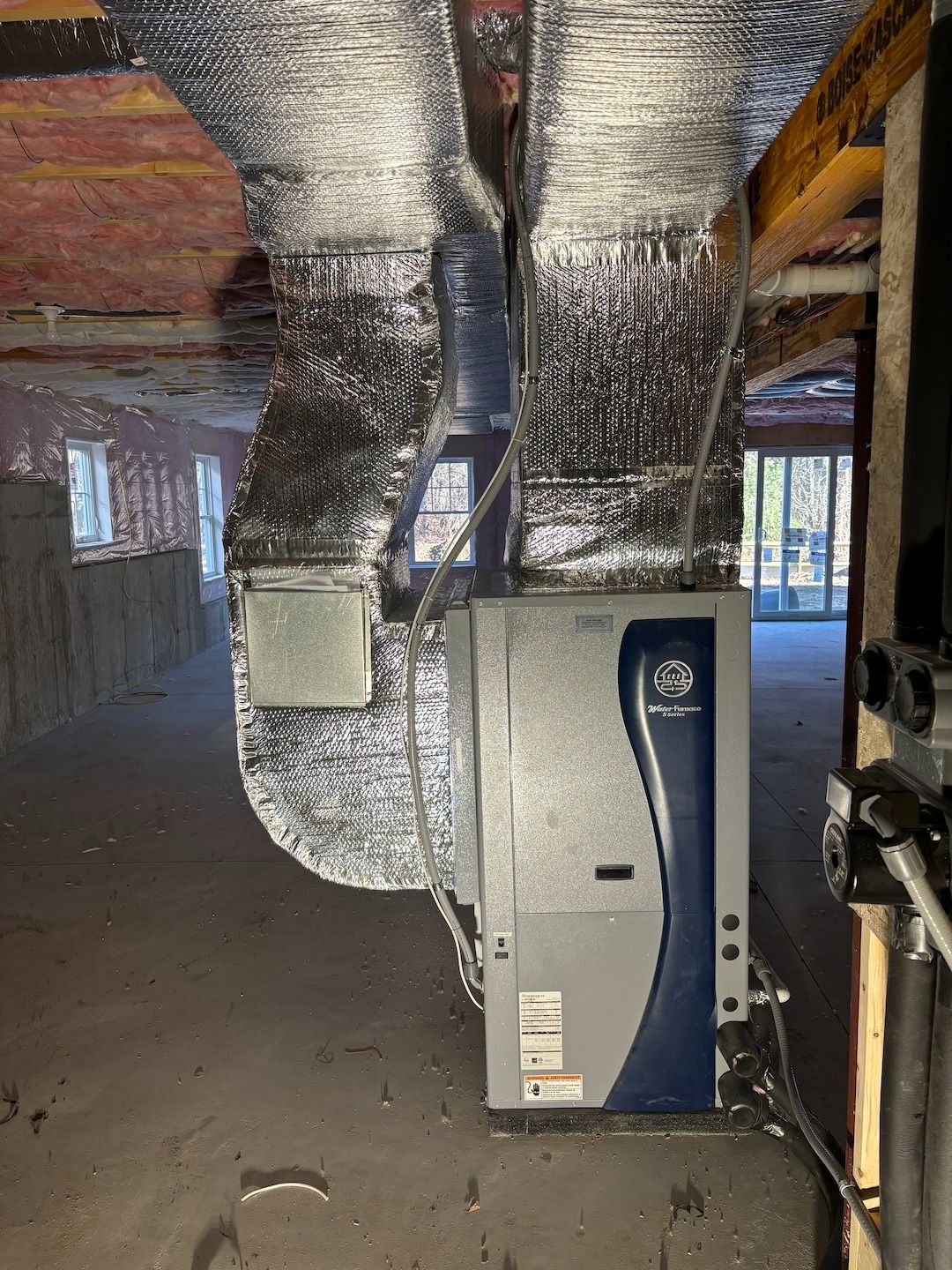 Basement HVAC unit with silver ductwork and blue paneling in a partially finished room.
