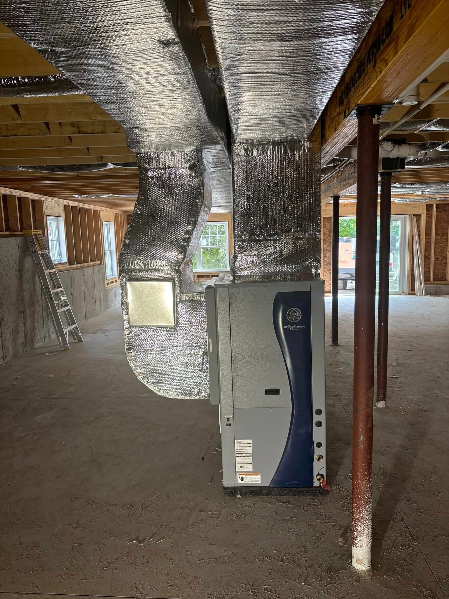 Basement under construction with exposed ductwork, insulation, and a white HVAC unit in the center.
