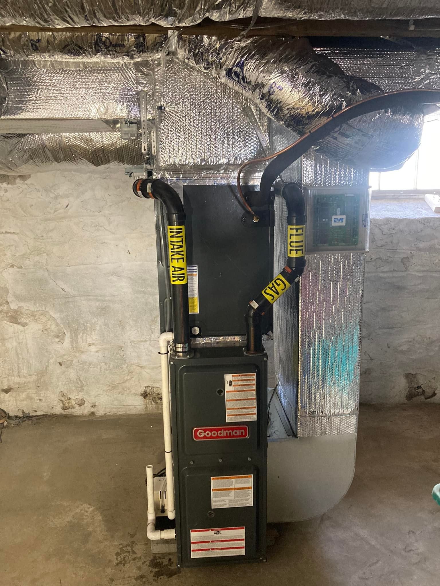 Gray HVAC unit with yellow warning straps in a basement beside a wall and exposed ductwork