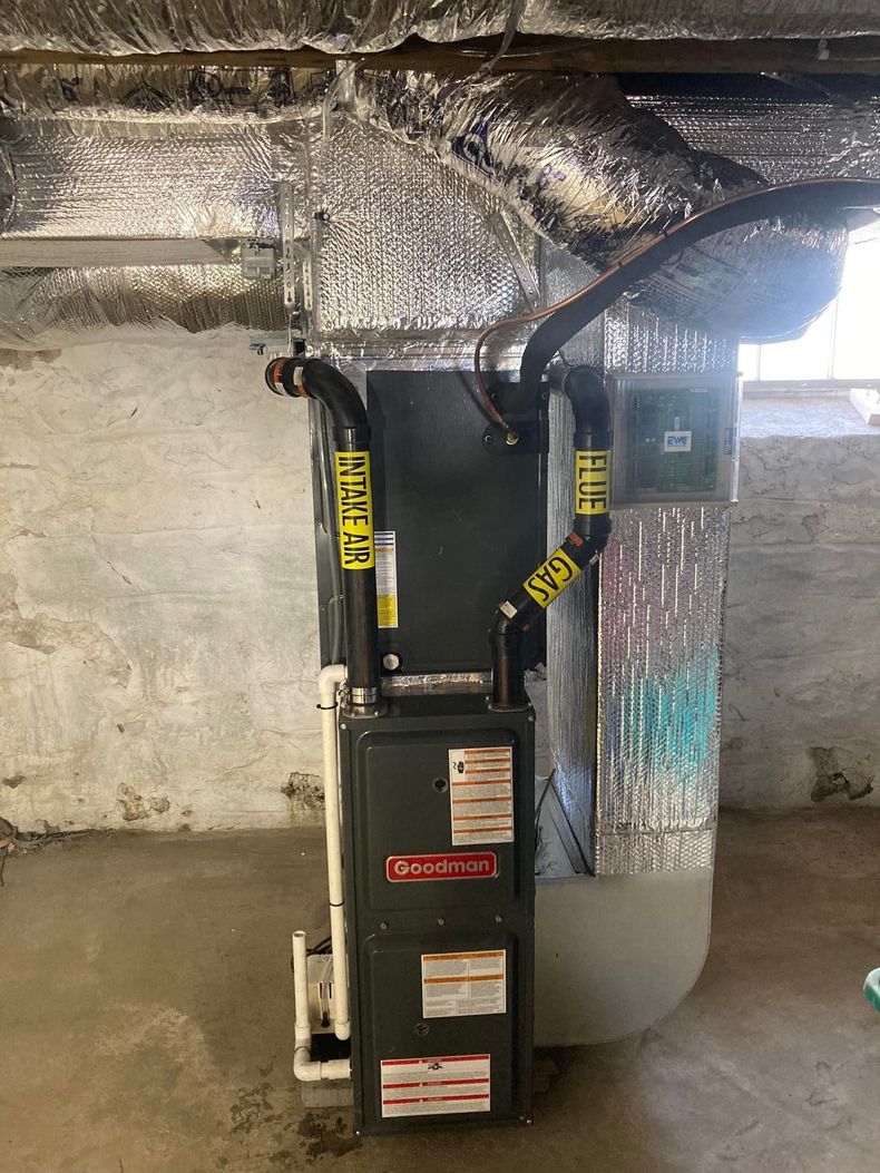 Gray HVAC unit with yellow warning straps in a basement beside a wall and exposed ductwork