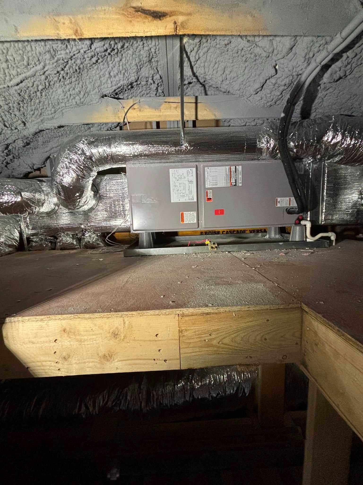 Metal HVAC equipment and ductwork in an attic crawl space beneath a wooden beam.