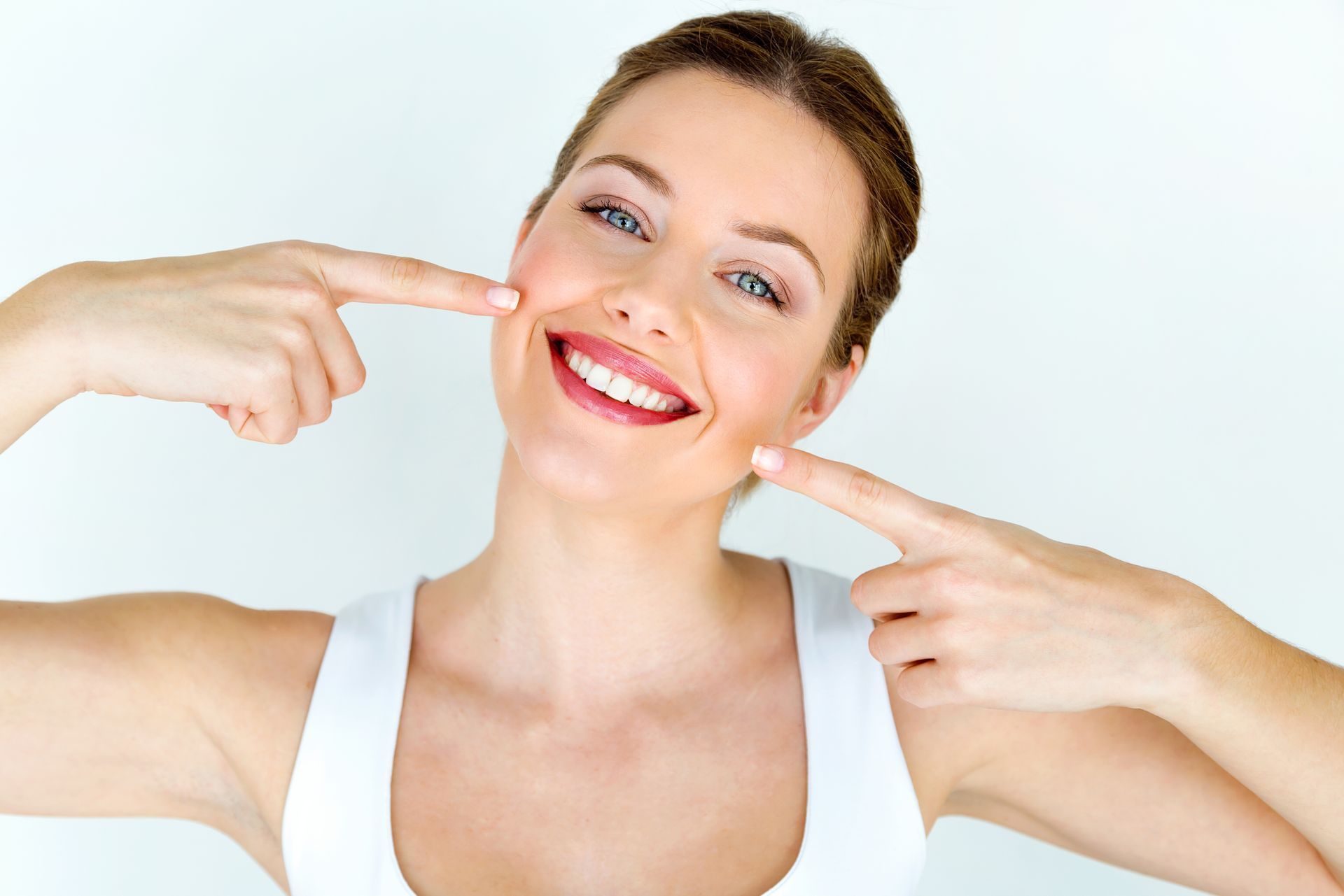 Visit our natural dentist for veneers, implants, root canals, and more in Morgantown WV A woman is smiling and pointing at her teeth.