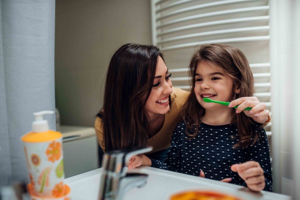 A woman is brushing her daughter 's teeth in the bathroom.