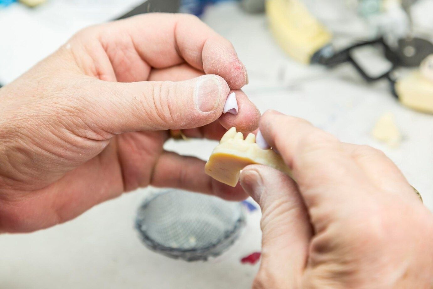 A dental technician is working on a model of a tooth.