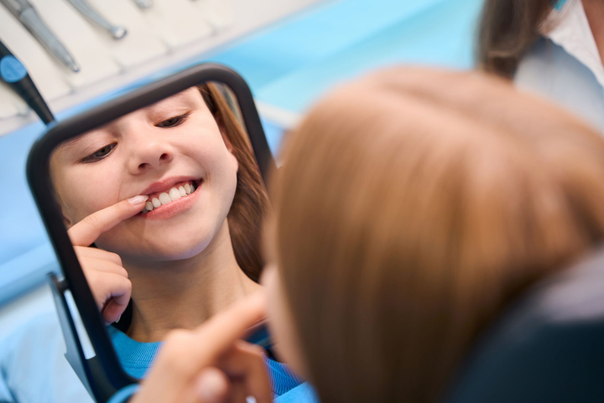 Person checking teeth in a mirror, smiling in a dental office with a dentist nearby