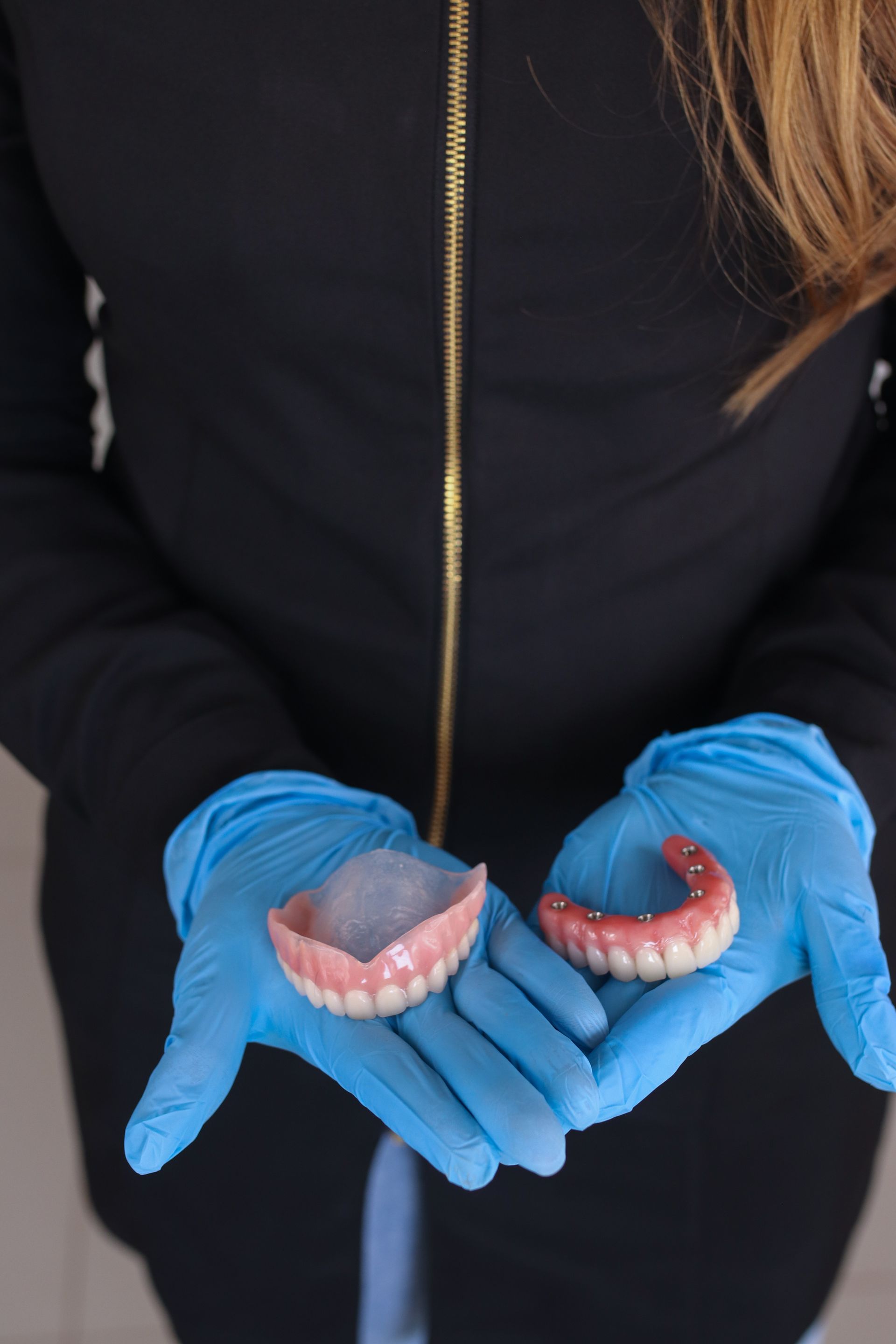 Get conventional or implant supported dentures from our top biodentist in Morgantown WV A woman wearing blue gloves is holding two dentures in her hands.