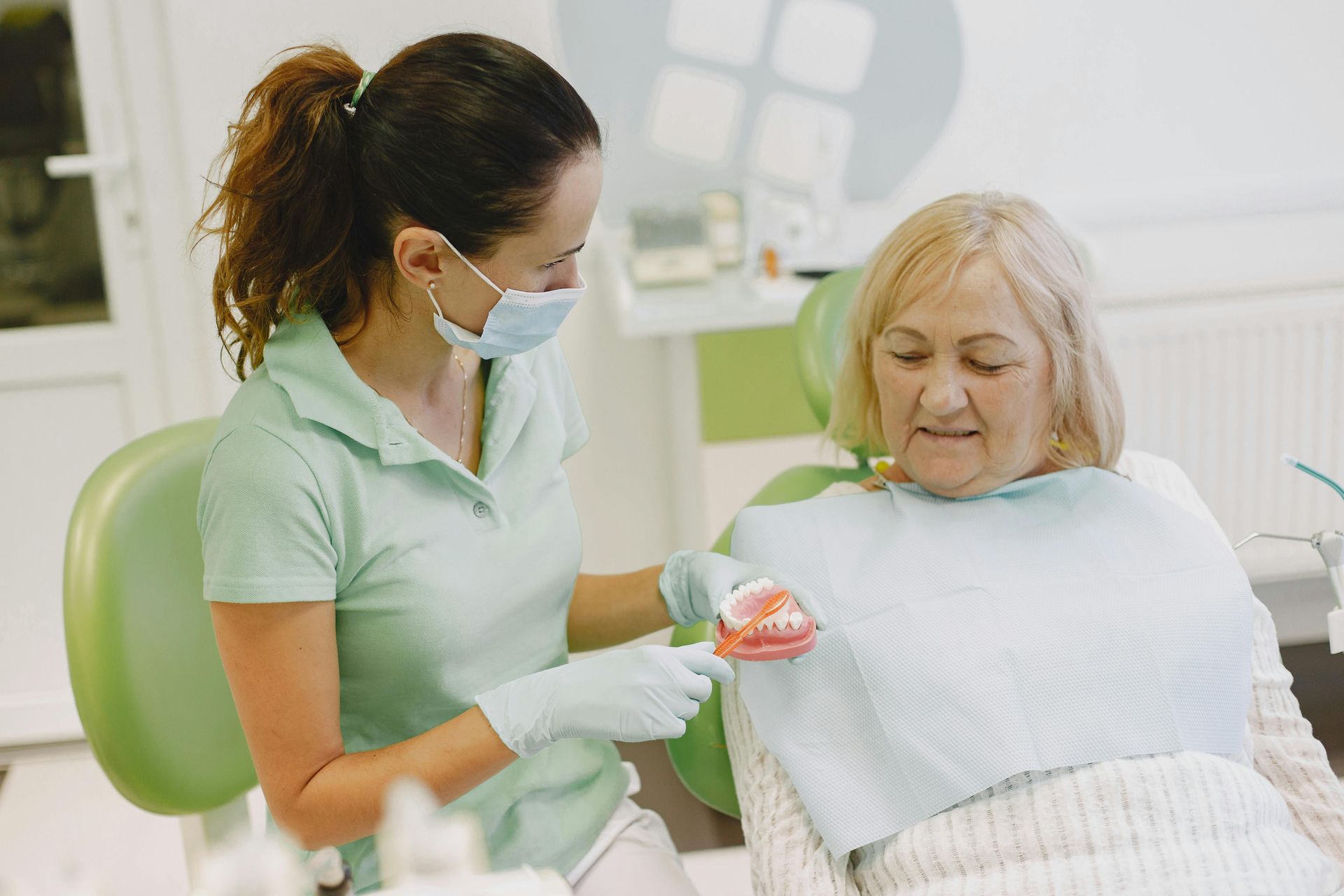 Dental assistant showing patient a model of teeth, discussing details of treatment and how it helps