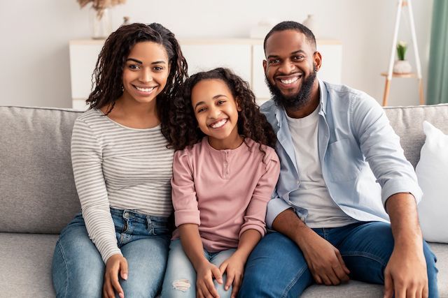 A family is sitting on a couch together and smiling for the camera.