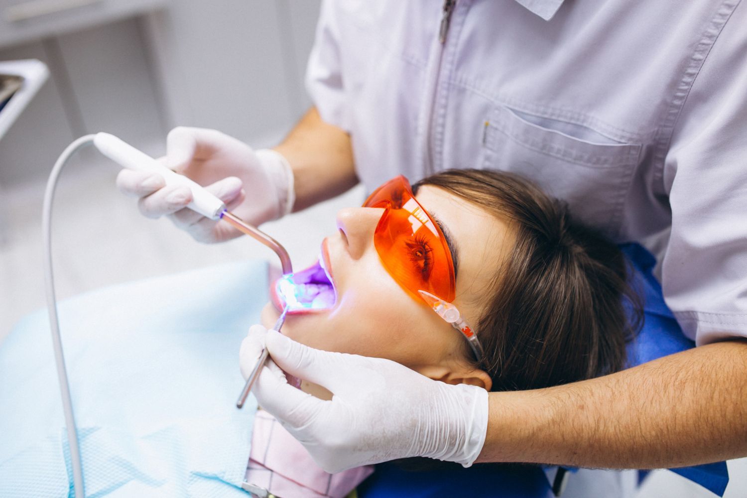 A woman is getting her teeth whitened by a dentist in a dental office.