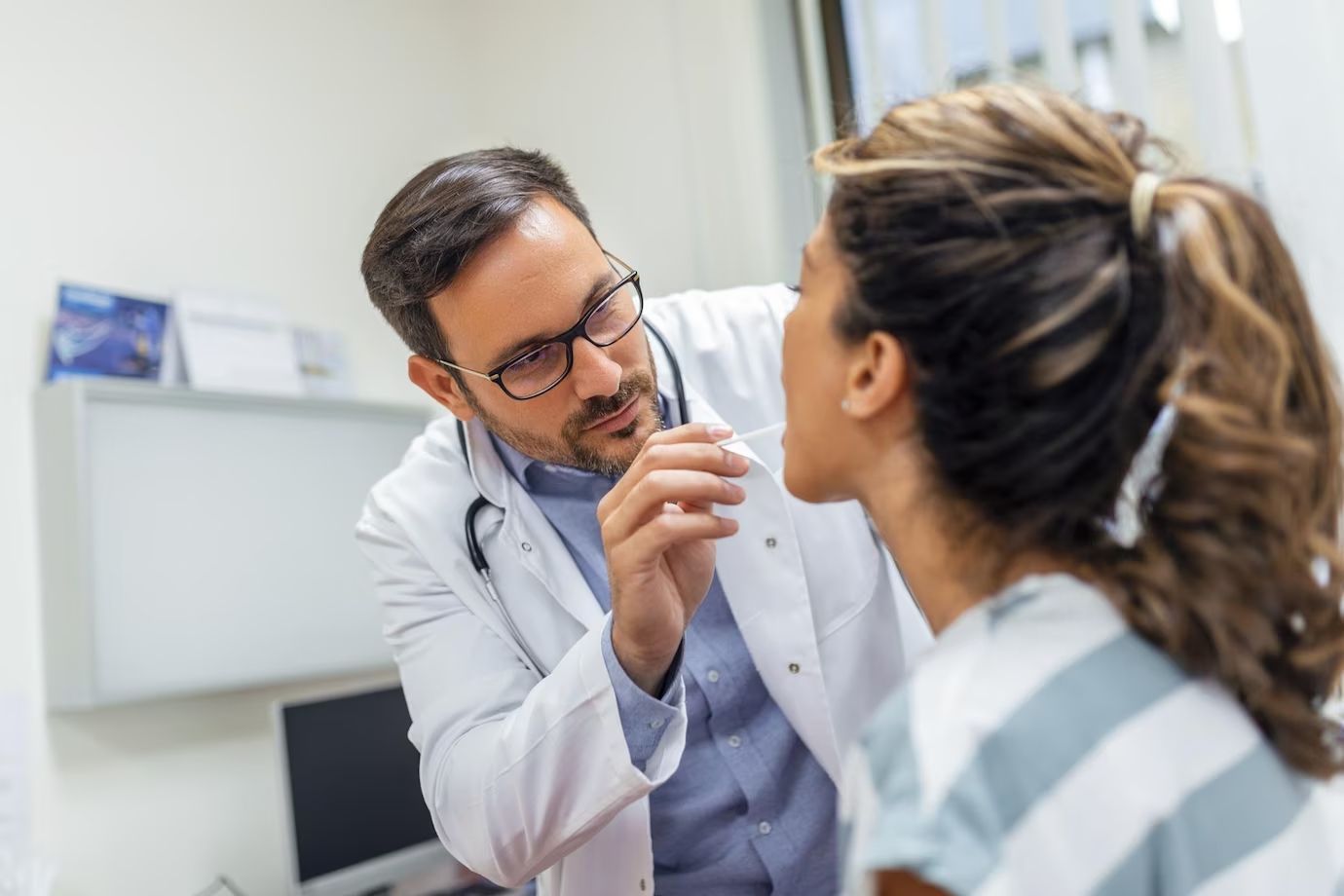 A doctor is examining a patient 's throat in an office.