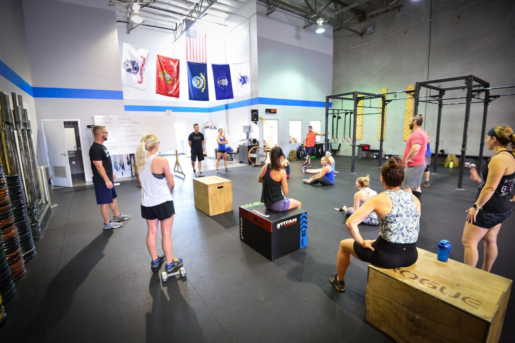 People resting during a CrossFit-style group workout in Iron Grip CrossFit, a gym in Tucson, AZwith rigs, boxes, and hanging flags.