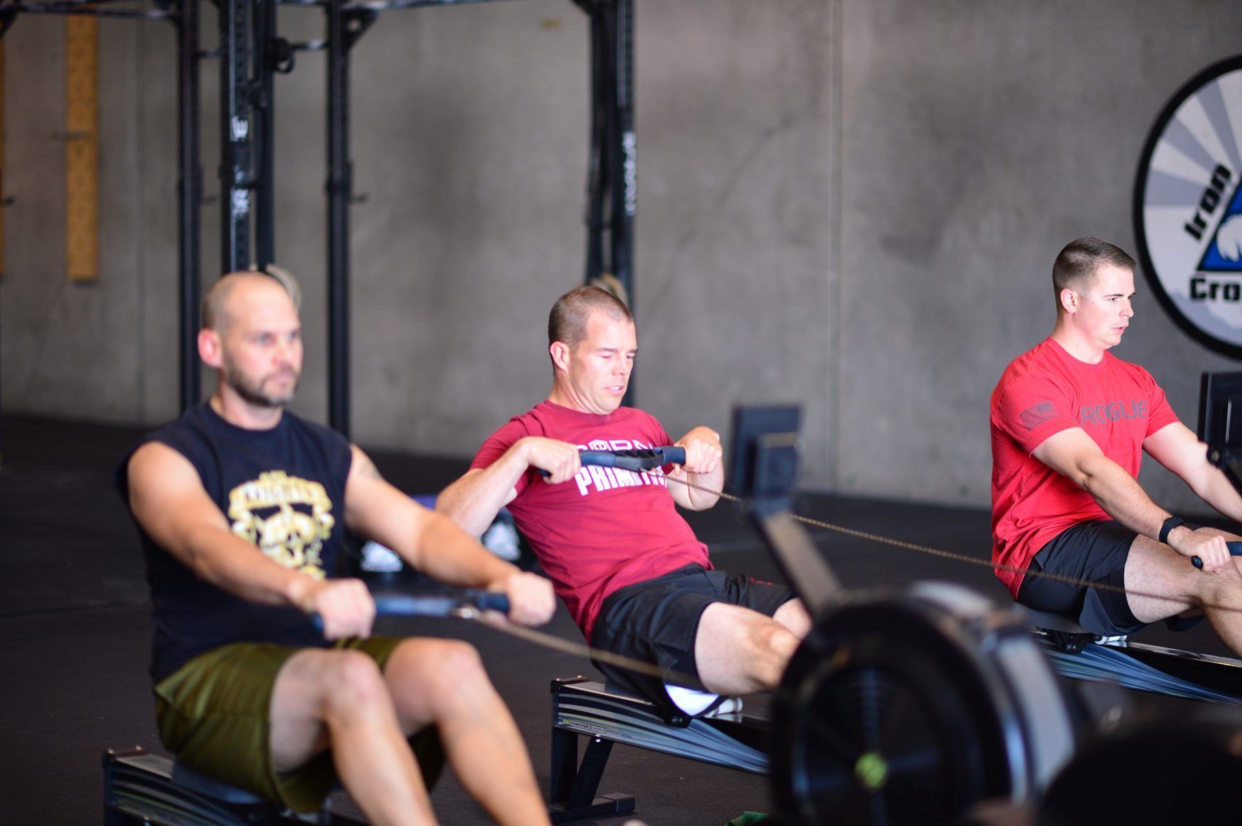 Three men exercising on rowing machines Iron Grip CrossFit, a gym in Tucson, AZ, with focused expressions.