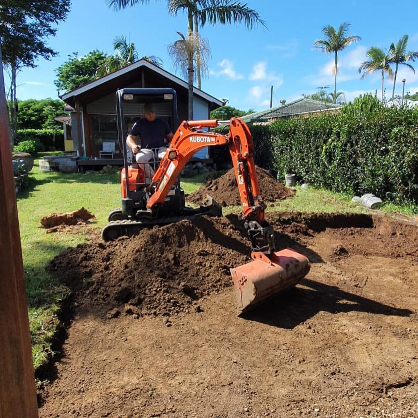 Man Operating An Orange Excavator, Digging In A Dirt Patch In A Backyard — Lifestyle Demolition In Byron Bay, NSW