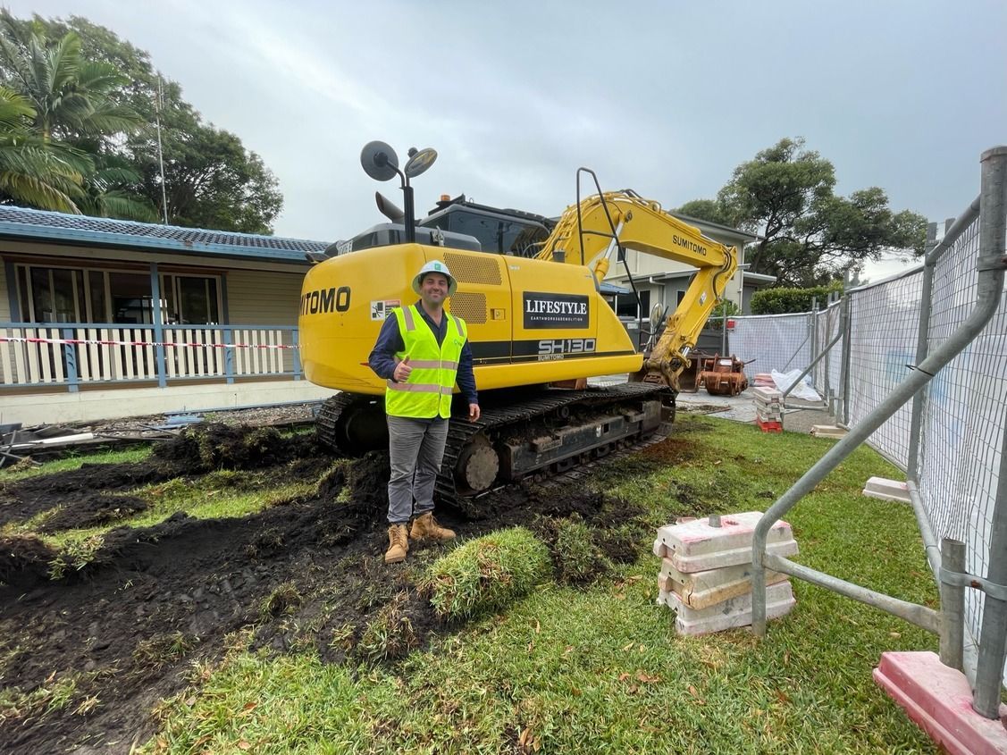 A Man Is Standing in Front of A Large Yellow Excavator — Lifestyle Demolition in Kingscliff, NSW