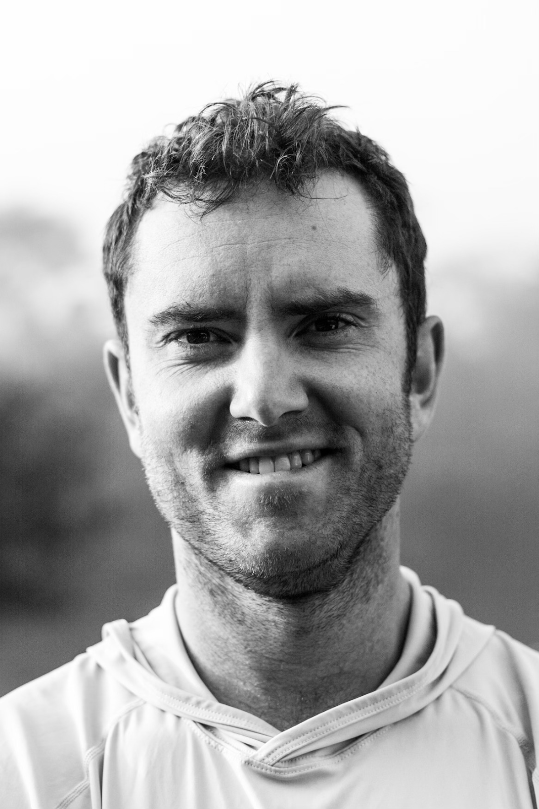 A man with a beard is smiling in a black and white photo.