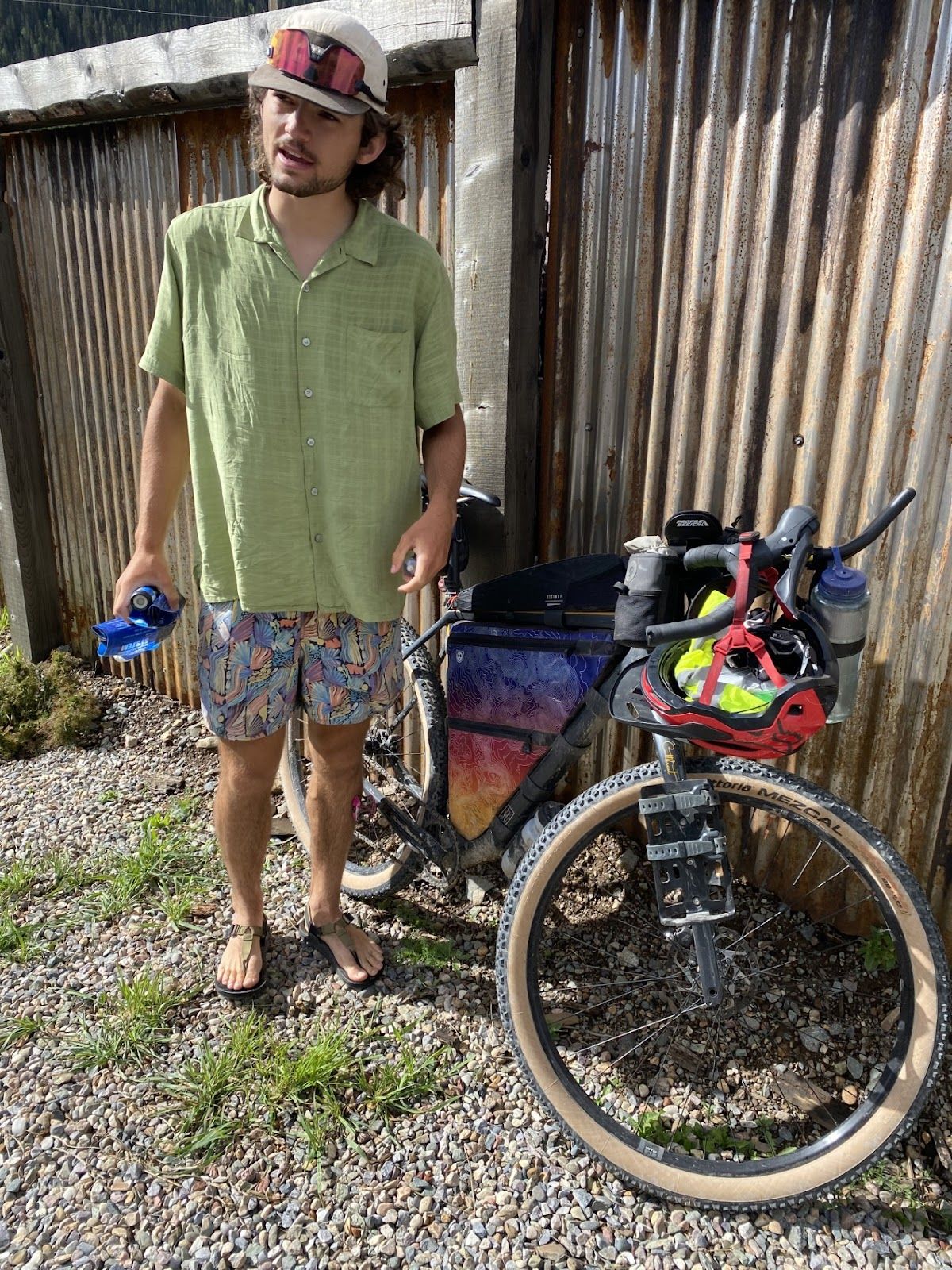A man is standing next to a bicycle on a gravel road.