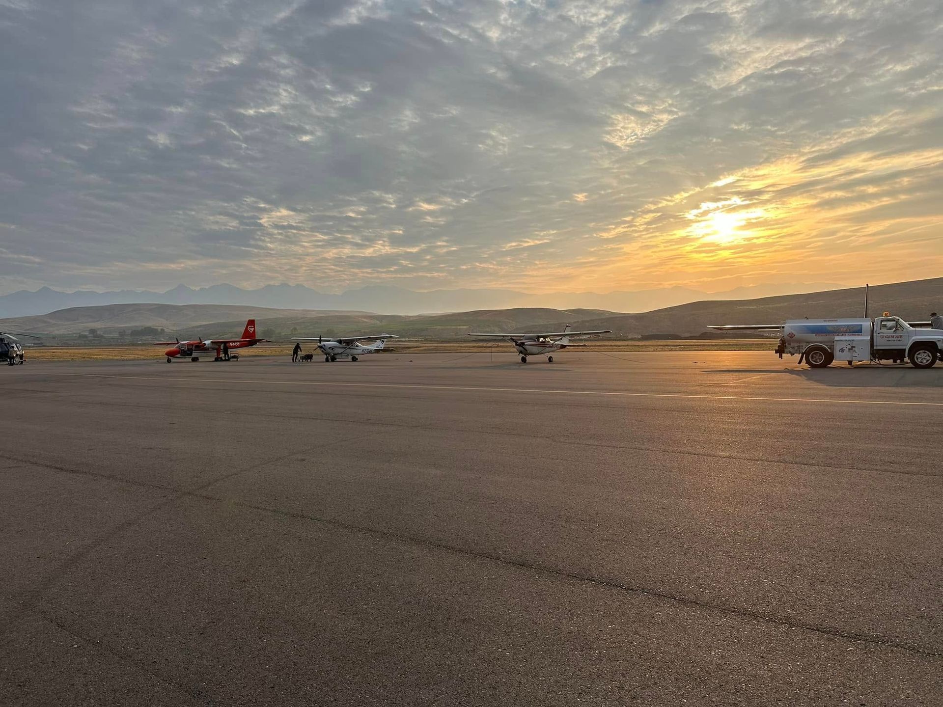 A row of planes are parked on an airport runway at sunset.