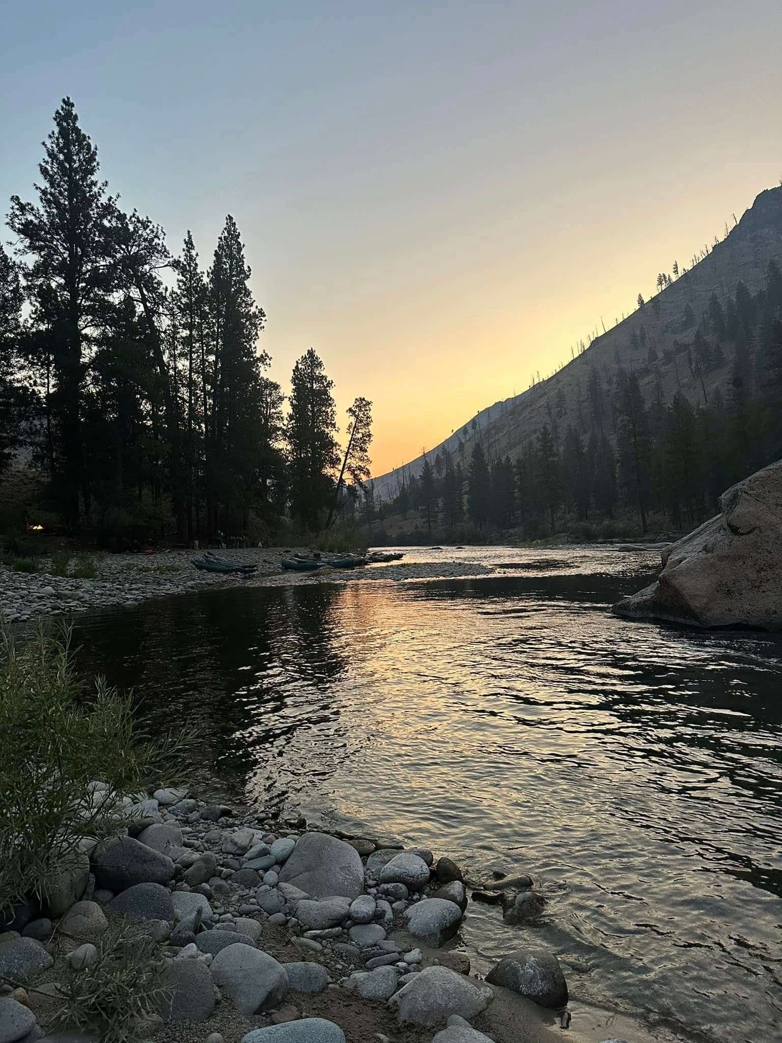 A river surrounded by trees and rocks at sunset.