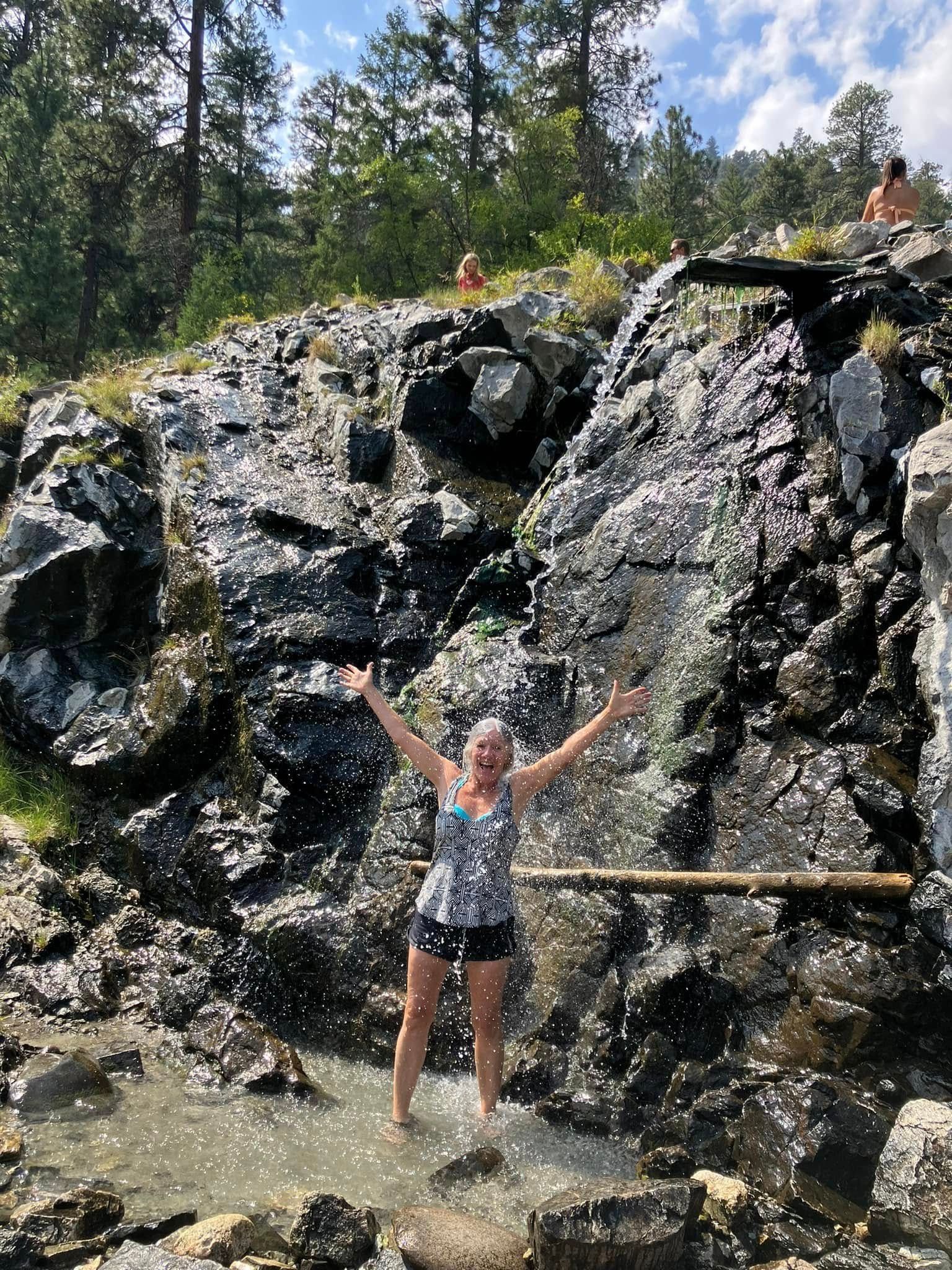 A woman is standing in front of a waterfall with her arms outstretched.