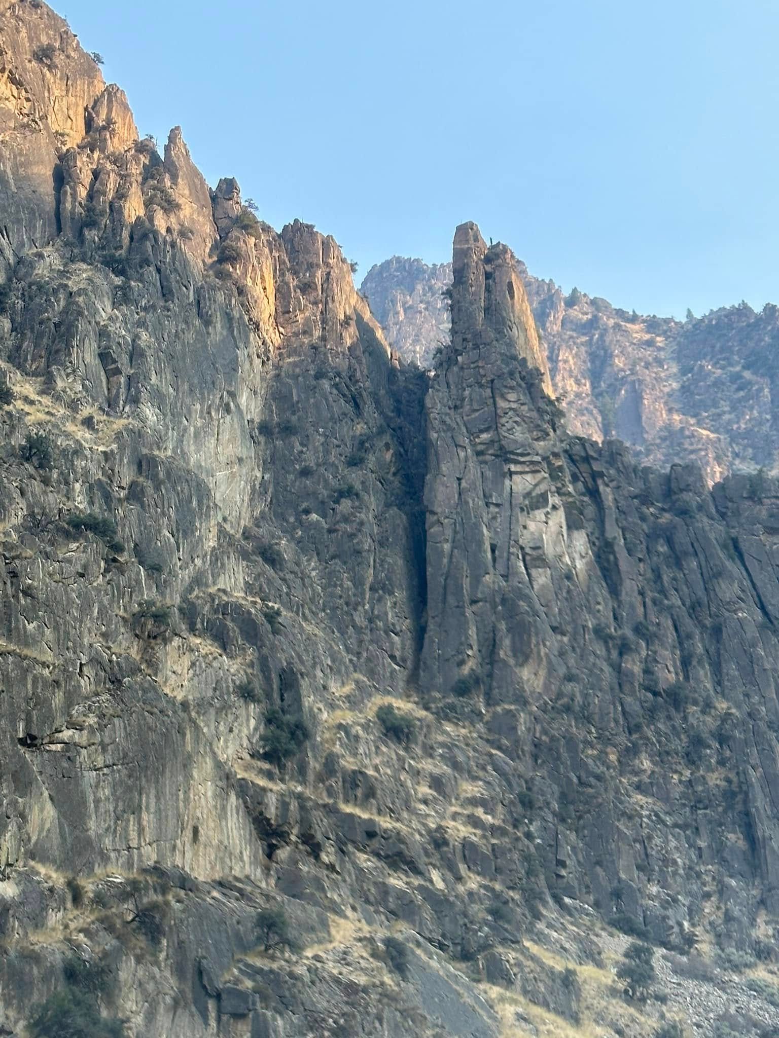 A mountain covered in trees and rocks with a blue sky in the background.