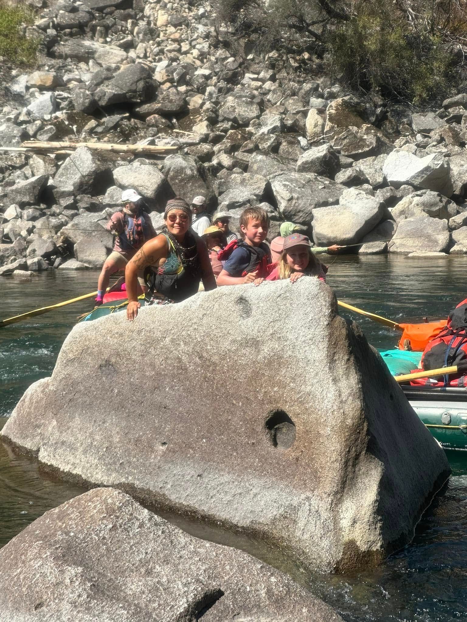 A group of people are sitting on top of a large rock in the water.
