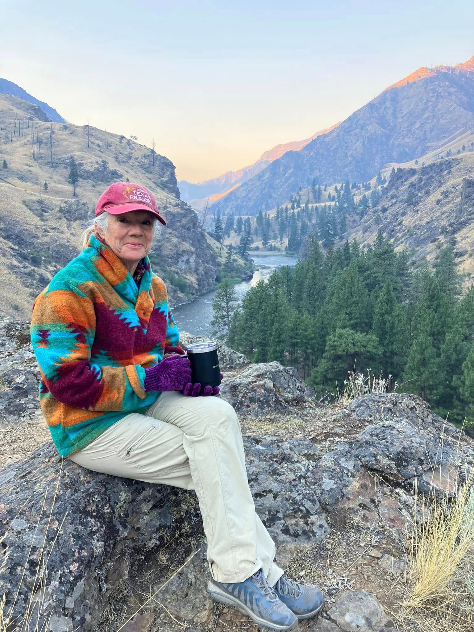 A woman is sitting on a rock holding a cup of coffee.
