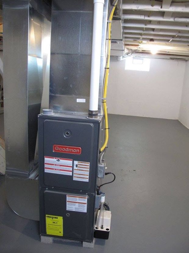 Basement furnace and ductwork in a utility room with exposed pipes and concrete floor