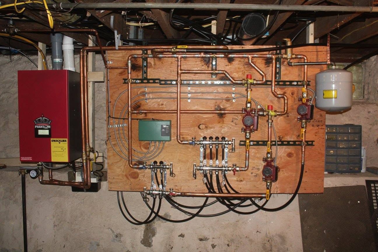 Industrial boiler control panel with red electrical box, copper piping, gauges, and wires on a basement wall