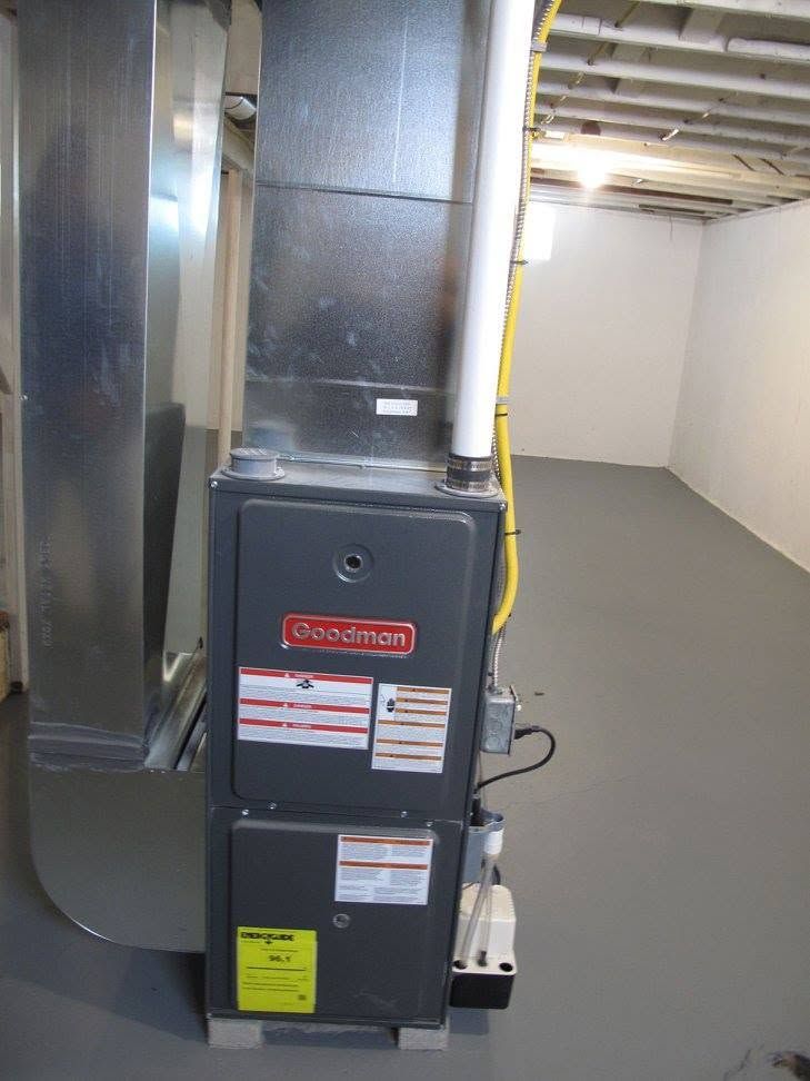 Gray industrial HVAC furnace in a basement beside metal ductwork and yellow piping