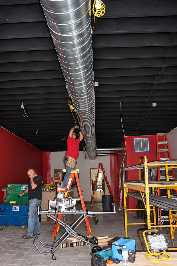 People installing ductwork on ladders in a red-and-black industrial interior
