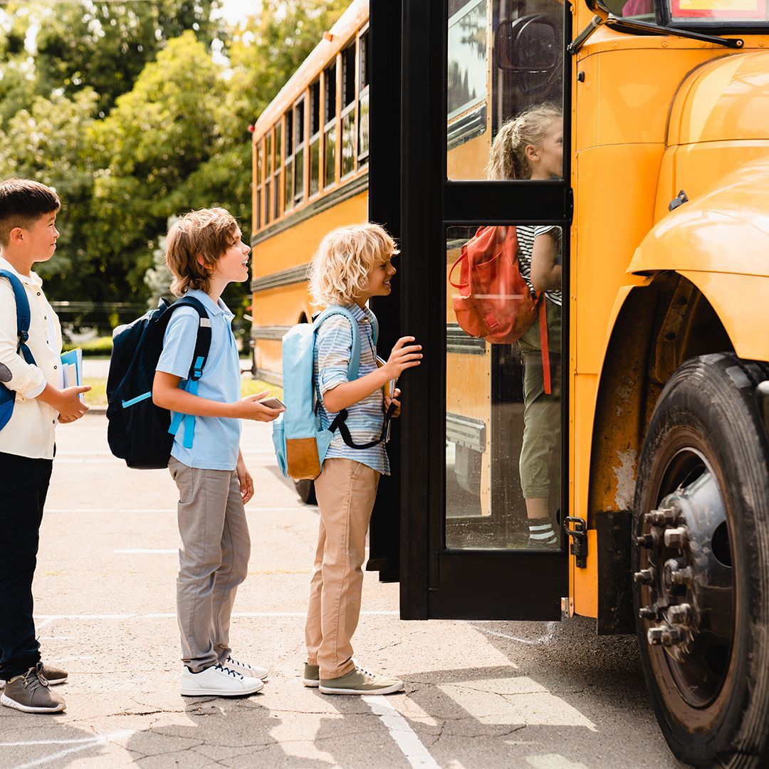 A group of children are standing next to a yellow school bus.