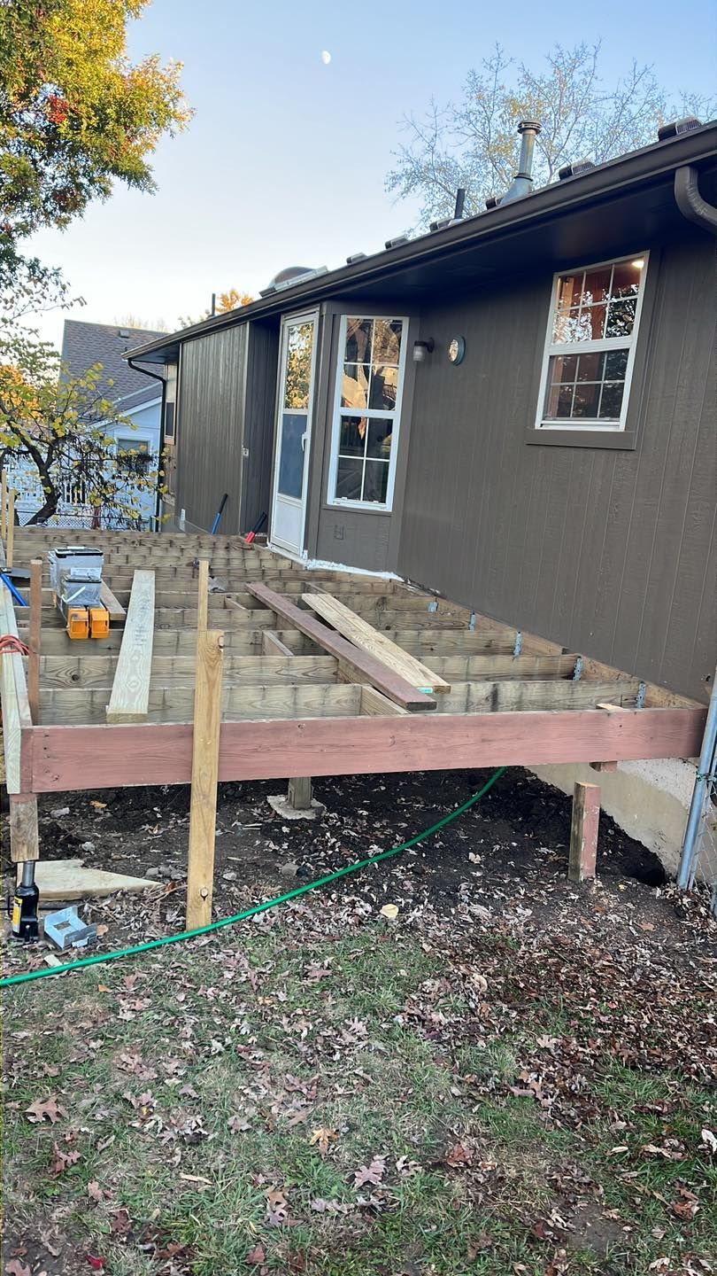 Deck under construction next to a house with brown siding. Brown and tan wood materials.
