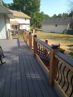 Wooden deck with black decorative railing, next to a house. Sunny, outdoor setting.