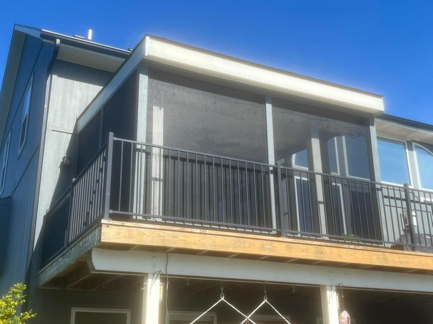 Black screened porch with black railing and light wood deck, attached to a gray house.