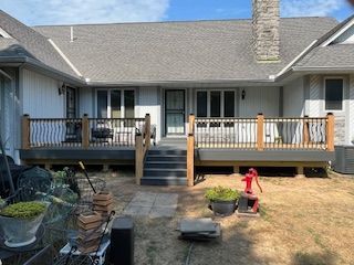 A house with a gray roof and a wooden deck; a set of stairs leads down to a backyard.