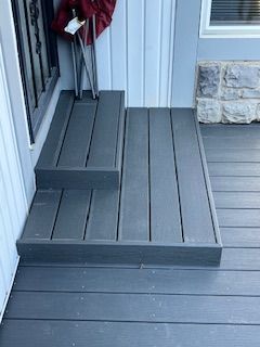 Gray composite deck with two steps leading to a door.  A red jacket and chair are on the deck.