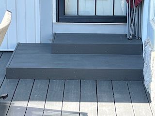 Grey composite deck with two steps leading to a door; small, folded chair.