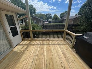 Wooden deck with black railing and grill, leading to a fenced backyard.