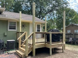 Wooden deck with black railing, steps, and posts. A grill sits on the deck. A house is in the background.