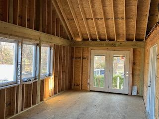 Interior of a room under construction; wooden frame walls, windows, and a door visible.