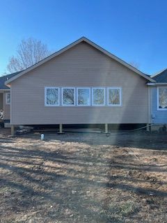 Back of a house with light brown siding, five white-framed windows, and a raised wooden foundation.